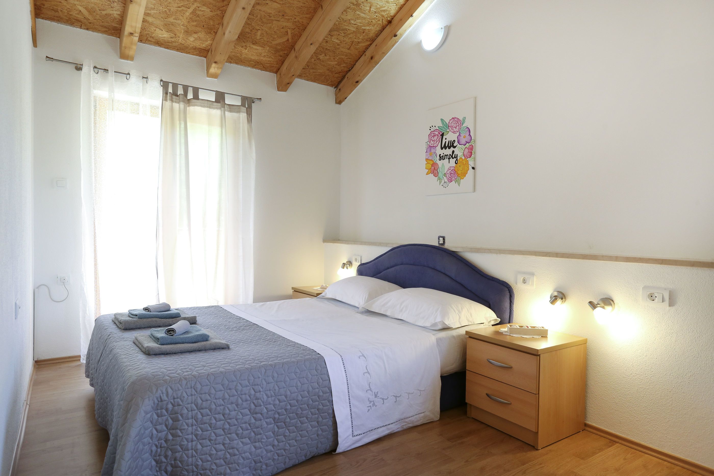 A bedroom with a bed, nightstands, a wooden dresser, and a ceiling with exposed beams.
