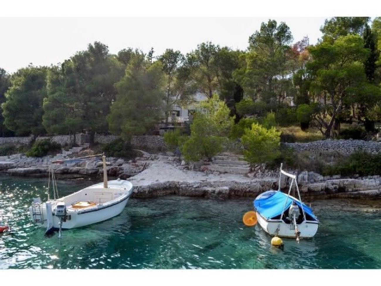 Two boats docked at a marina with rocky shores and trees in the background.