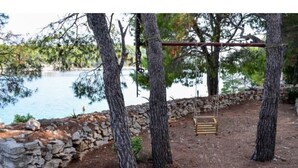 A rustic outdoor area with a stone wall, trees, and a wooden swing. - Apartment Ante (Milna)