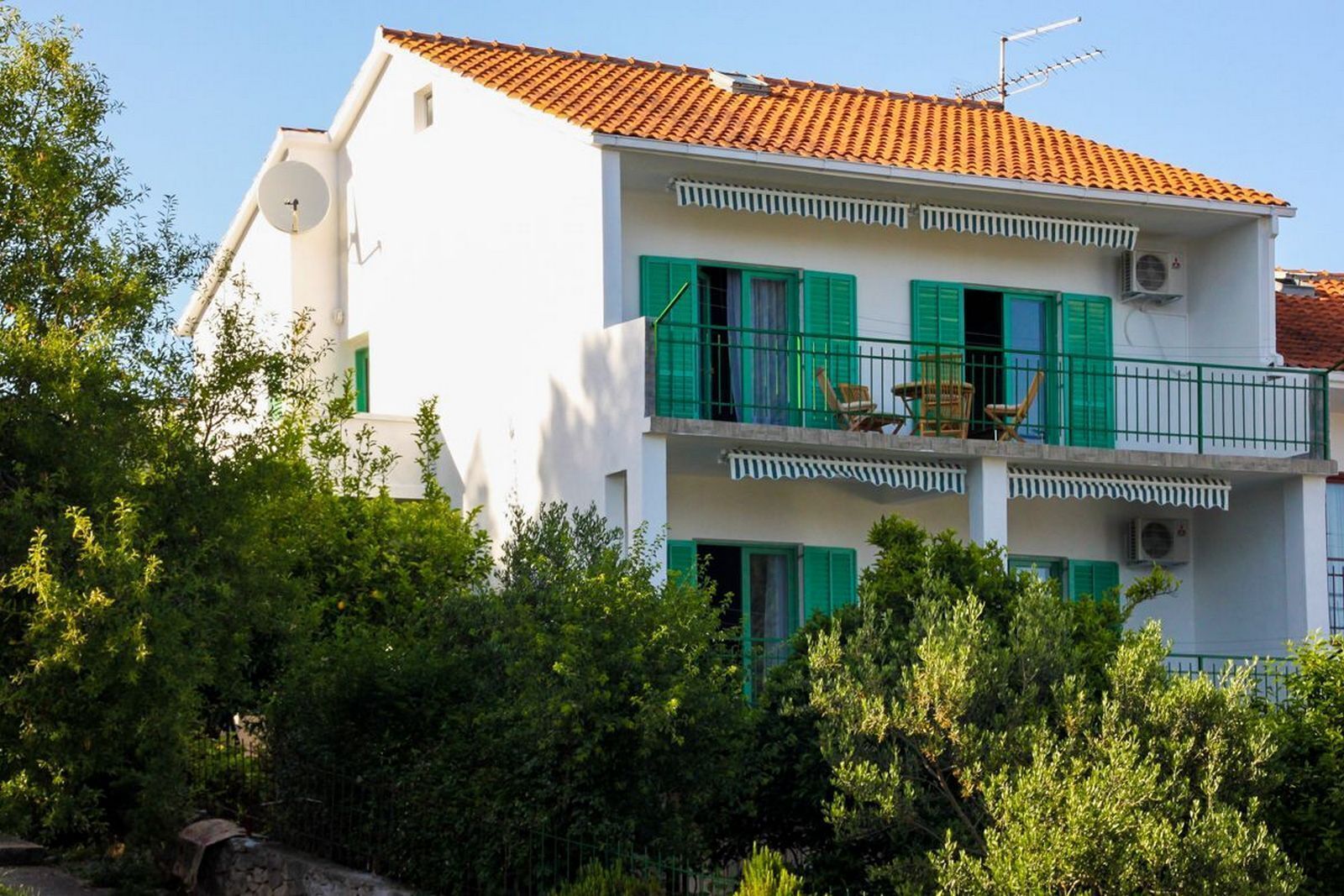 A two-story building with a red-tiled roof, white walls, and green shutters.