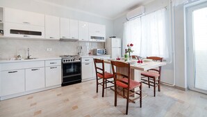 A modern kitchen with white cabinets, a stove, microwave, and a dining area with a table and chairs. - Apartments Andela (Brsec)