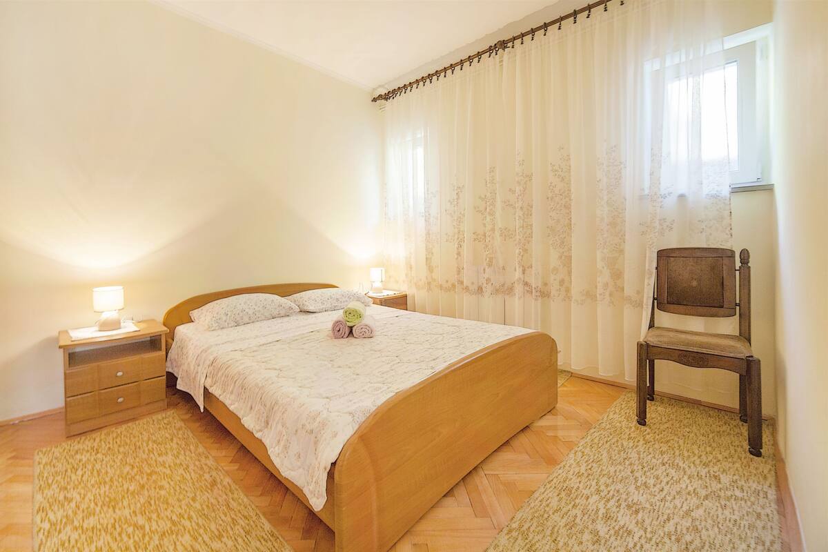 A bedroom with a bed, two bedside tables, a chair, and a window with curtains.