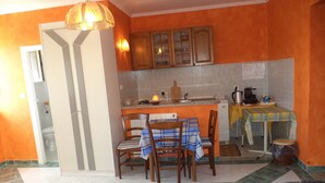 A kitchen with wooden cabinets, a dining table with chairs, a small island with a sink, and a refrigerator. - Apartments Andela (Brsec)