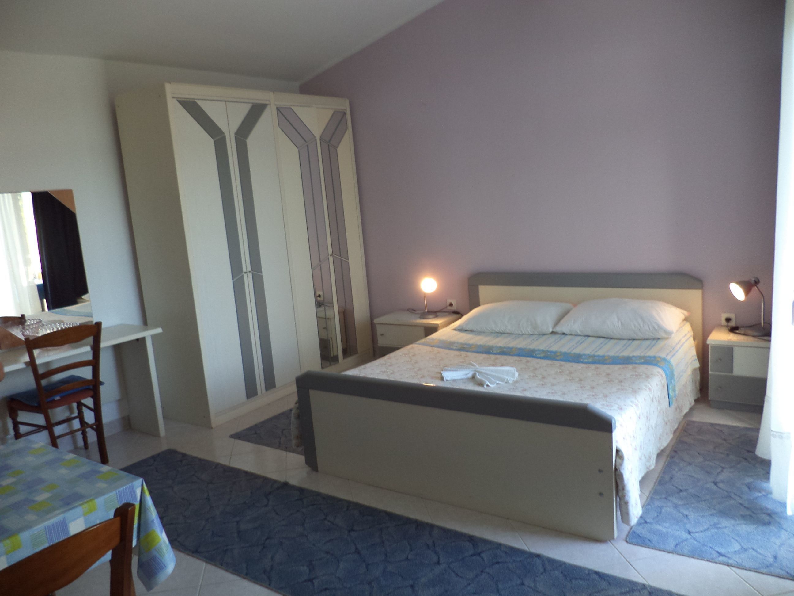A bedroom with a bed, bedside tables, a desk, a chair, and a wardrobe.