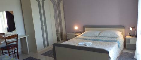 A bedroom with a bed, bedside tables, a desk, a chair, and a wardrobe.