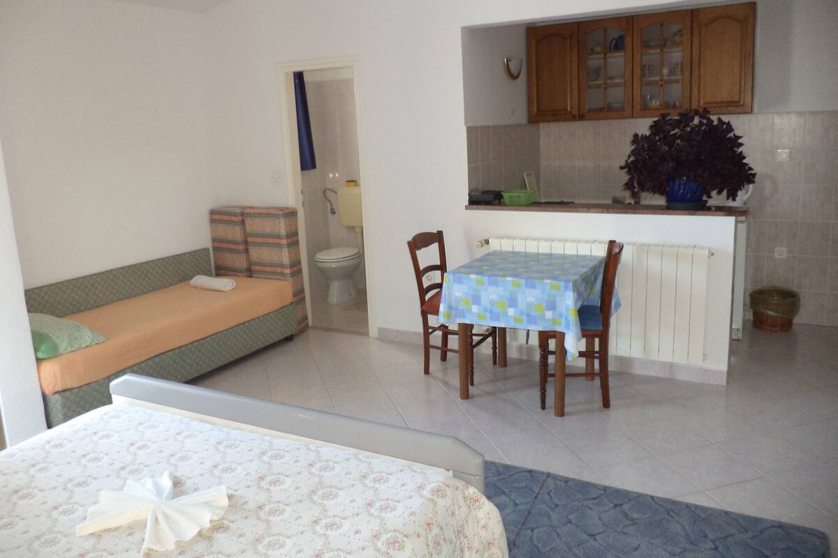 A compact room with a bed, a small kitchenette, a dining table with chairs, and a bathroom.