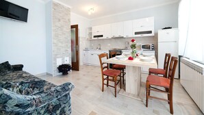 A modern kitchen with white cabinets, a dining table set for four, and a small island. - Apartments Andela (Brsec)