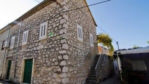 Un bâtiment en pierre avec une porte verte et des volets blancs, doté d’un escalier menant à un étage supérieur.