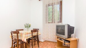 Ein Essbereich mit einem Tisch für vier Personen, einem Fernseher auf einem Holzgestell und einem Spitzenvorhang.