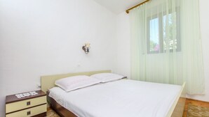 Ein Schlafzimmer mit einem Bett, einem Nachttisch, einer Wandlampe und einem Fenster mit Vorhängen.