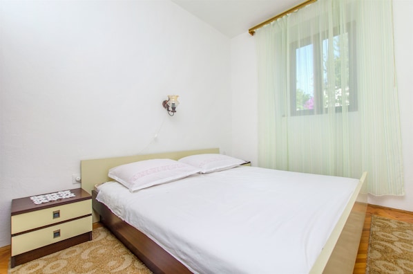 Un dormitorio con una cama, una mesita de noche, una lámpara de pared y un ventanal con cortinas.