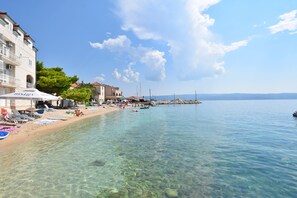 A coastal beach scene with clear water, a sandy shore, and buildings along the water's edge. - Apartments Zanet (Sumpetar)