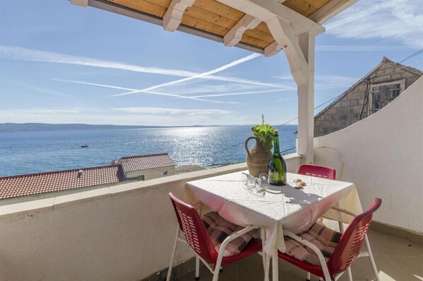 A balcony with a table and chairs, overlooking a body of water with a clear sky.