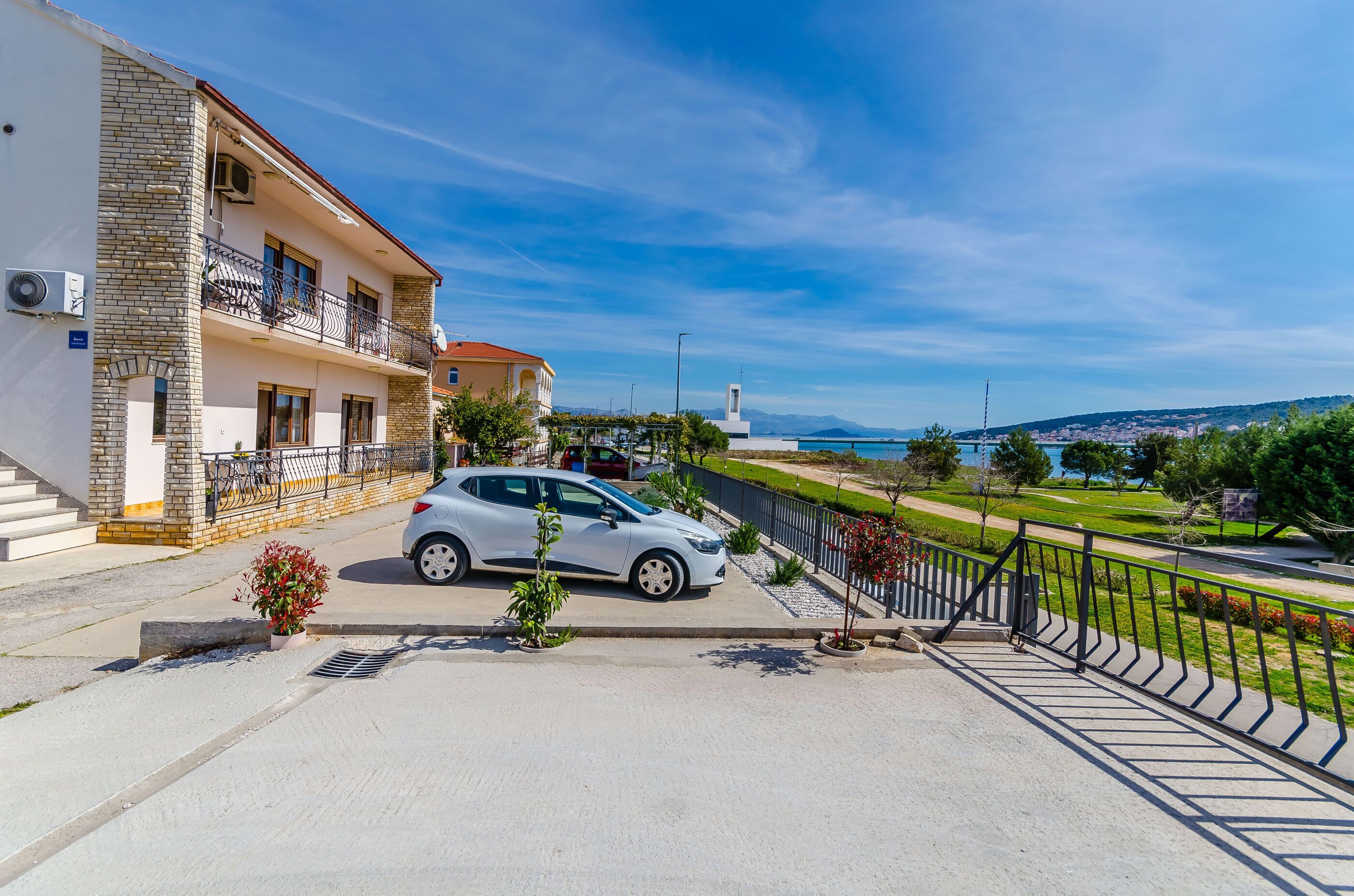 Edificio residencial con un coche estacionado adelante, un balcón y vista al mar.