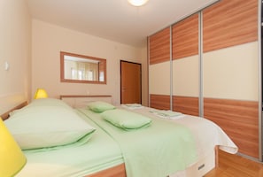 Een slaapkamer met een bed, nachtkastje, spiegel, kledingkast en lamp.