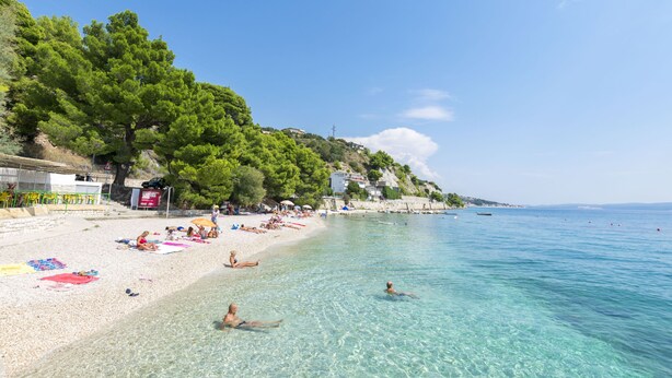 Una playa con agua cristalina, gente tomando el sol y algunas embarcaciones.