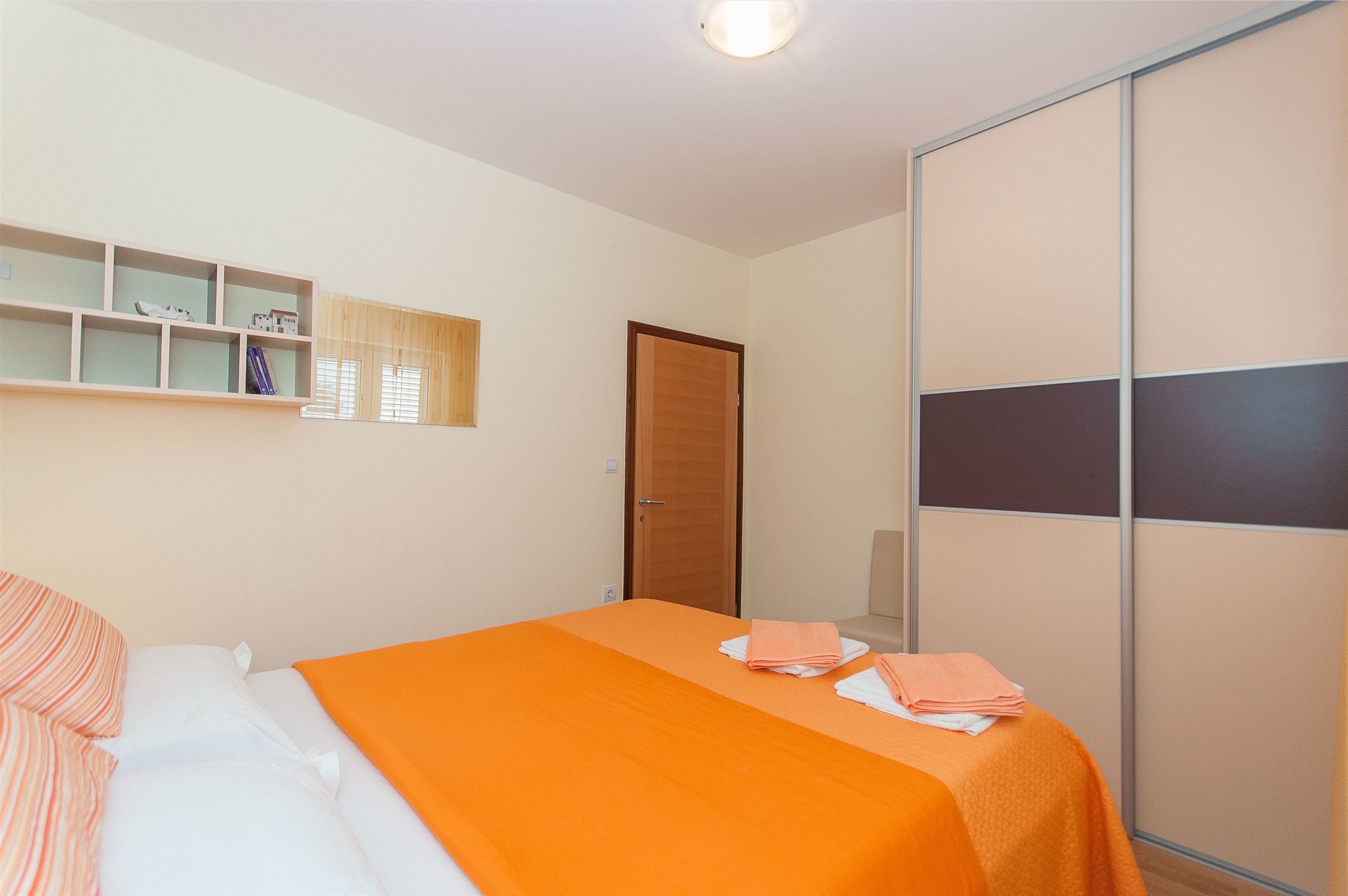Una habitación de hotel con cama, armario, estante con libros y ventana con persianas.