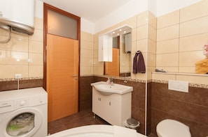 Een badkamer met een wasmachine, een wastafel, een spiegel en een toilet.