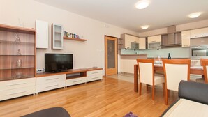 Una sala de estar moderna con un televisor de pantalla plana, estanterías de madera y un comedor con mesa y sillas.