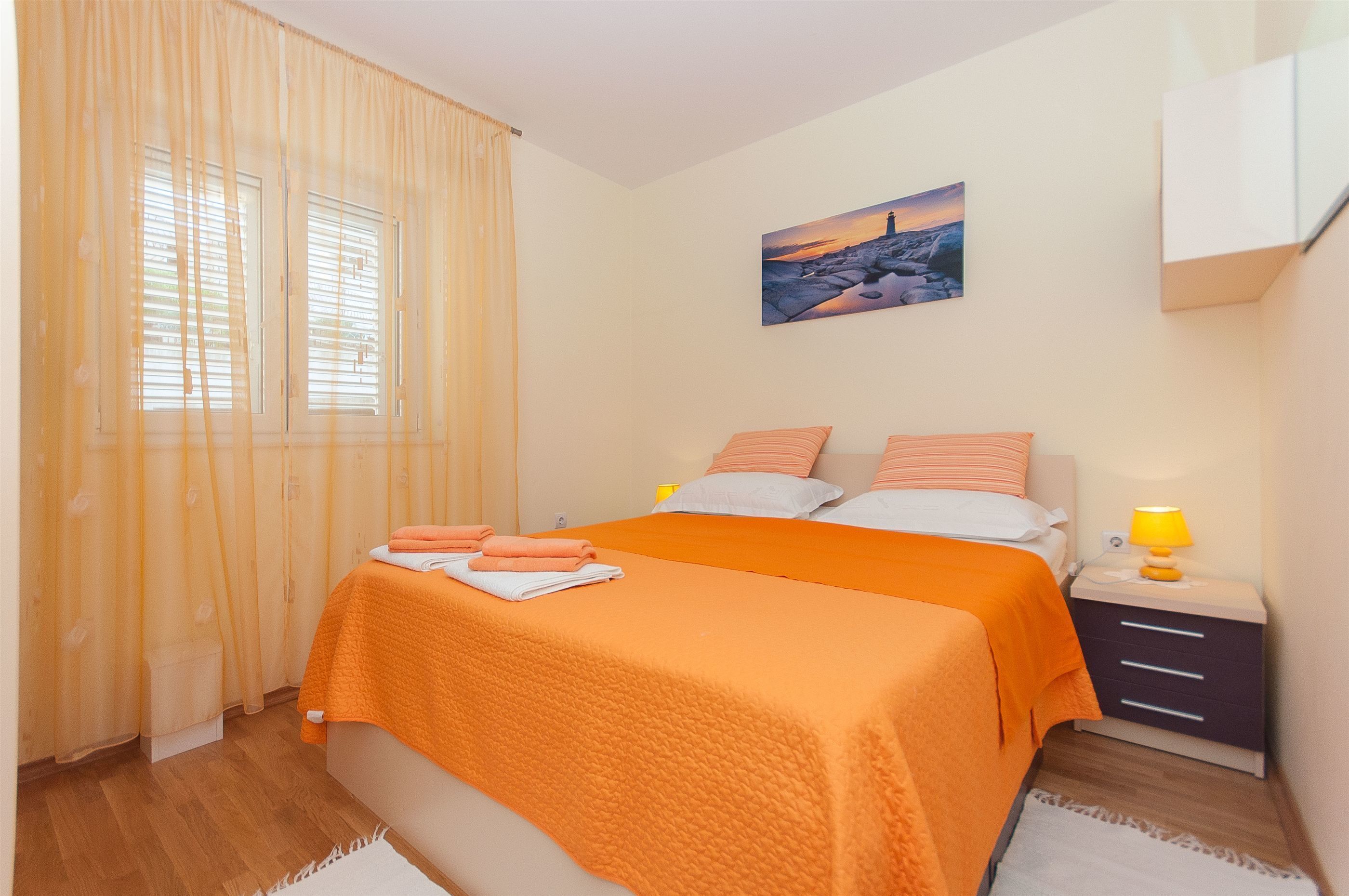 Une chambre à coucher avec un lit, des rideaux, une table de chevet, une lampe et un tableau au mur.