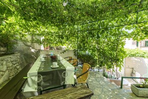 Area pranzo all'aperto con tavolo apparecchiato per quattro, circondata da mura in pietra e coperta da una fitta vegetazione.