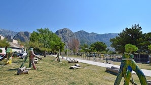A park with sculptures, a playground, and mountains in the background. - Apartments Mira (Omis)