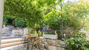 A stone-floored patio with a table and chairs, surrounded by lush greenery and potted plants. - Apartments Mira (Omis)