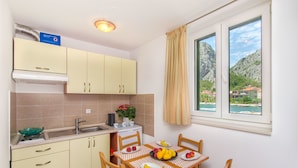 A compact kitchen with a dining area, a window with a mountain view, and a table set with fruit. - Apartments Mira (Omis)