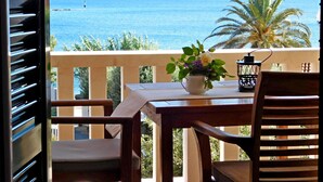 A balcony with a wooden table, two chairs, a vase with flowers, and a lantern. A view of the sea and a distant hill is visible through the railing. - Apartments Mirjana (Milna)