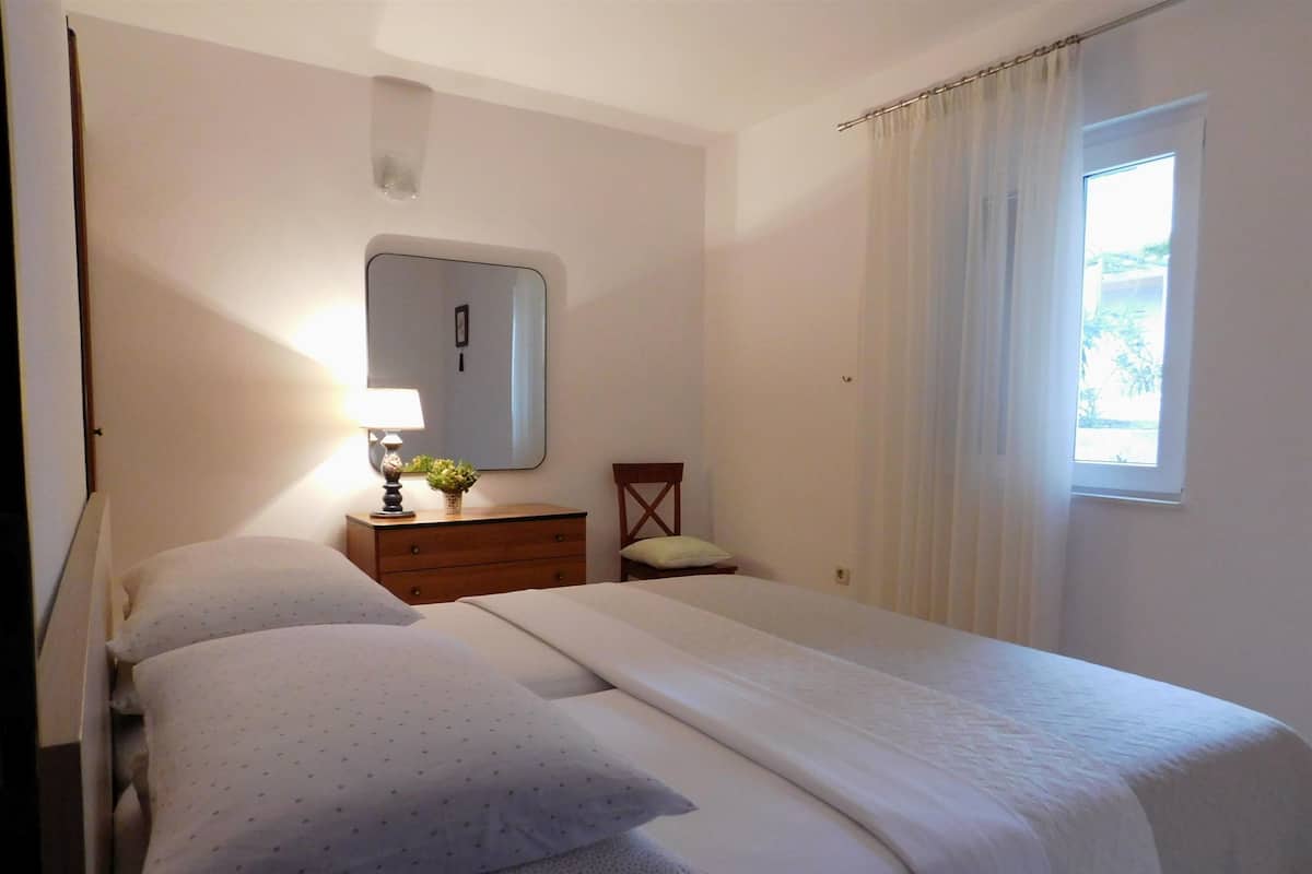 Un dormitorio con cama, mesita de noche, espejo y ventana con cortinas.