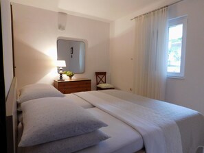 Un dormitorio con cama, mesita de noche, espejo y ventana con cortinas.