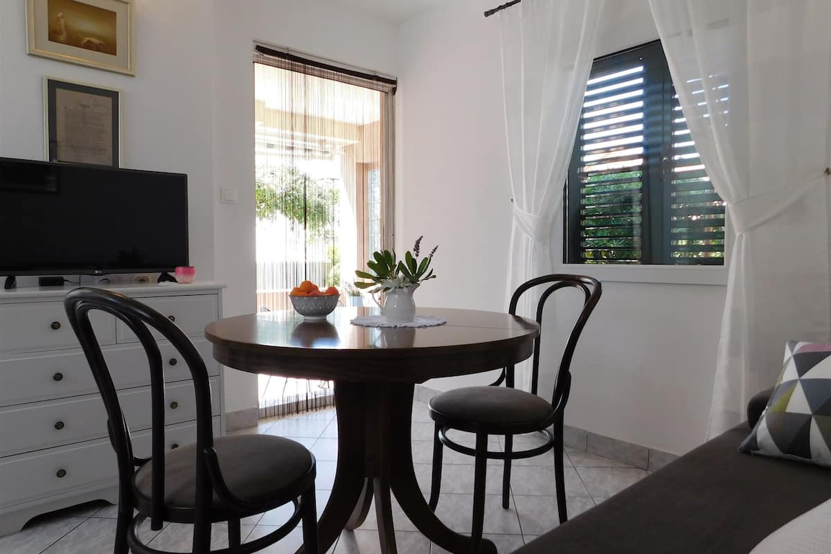 Un comedor con una mesa redonda, dos sillas, un cuenco de fruta y una planta en maceta.