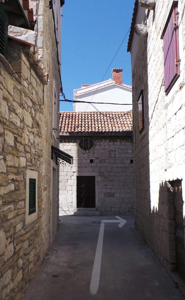 A narrow alleyway with stone buildings, a tiled roof, and a directional arrow on the ground.