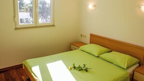 A bedroom with a single bed, a nightstand, a bedside table, a window, and a wall-mounted light fixture. - Apartment Marin (Trogir)