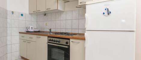 A compact kitchen with a gas stove, oven, and a white refrigerator.