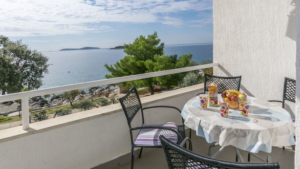A balcony with a table set for two, overlooking a scenic view of the sea and a distant island. - Apartments Gloria (Rogoznica)