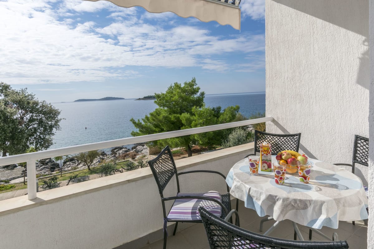 Un balcón con una mesa para dos, con vistas panorámicas al mar y una isla distante.