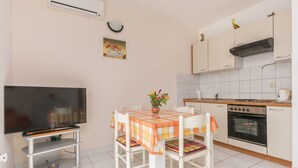 A compact kitchen with a dining table, chairs, a TV on a stand, an oven, and a tiled backsplash. - Apartments Gloria (Rogoznica)