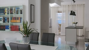 A modern living room with a glass dining table, black chairs, a bookshelf, and a potted plant. - Apartment Lucija (Supetar)