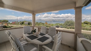 A covered outdoor seating area with a table and chairs, overlooking a scenic view of mountains and the sea. - Apartment Lucija (Supetar)