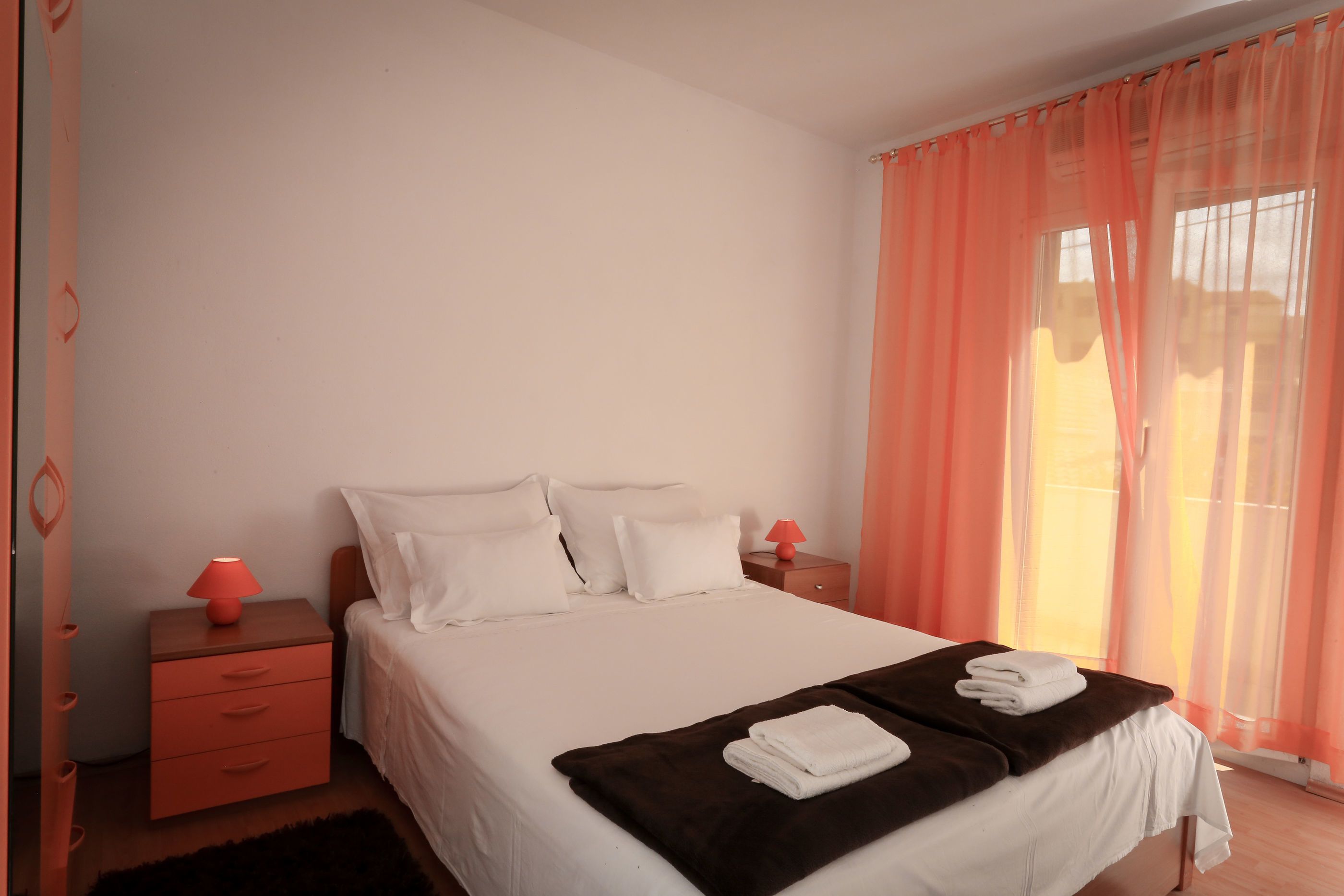 A bedroom with a bed, a nightstand, a lamp, and a window with curtains.
