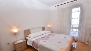Un dormitorio con cama, mesitas de noche, lámpara de pared y ventana con cortinas.