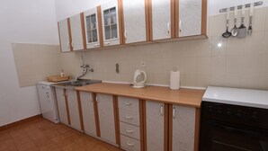Una cocina compacta equipada con lavavajillas, estufa y un lavamanos pequeño. Se observan armarios con un acabado similar al mármol y una encimera con escurreplatos.