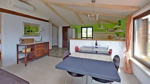 Un coin repas avec une table et des chaises, une cuisine en arrière-plan et une grande fenêtre avec des rideaux.
