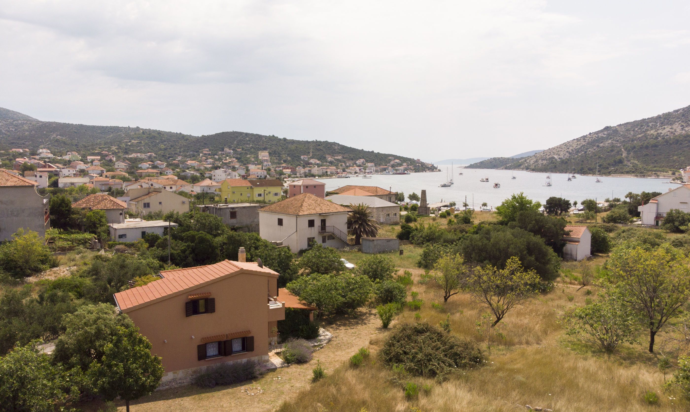 A coastal village with traditional houses, a clear view of the sea, and a hilly backdrop.