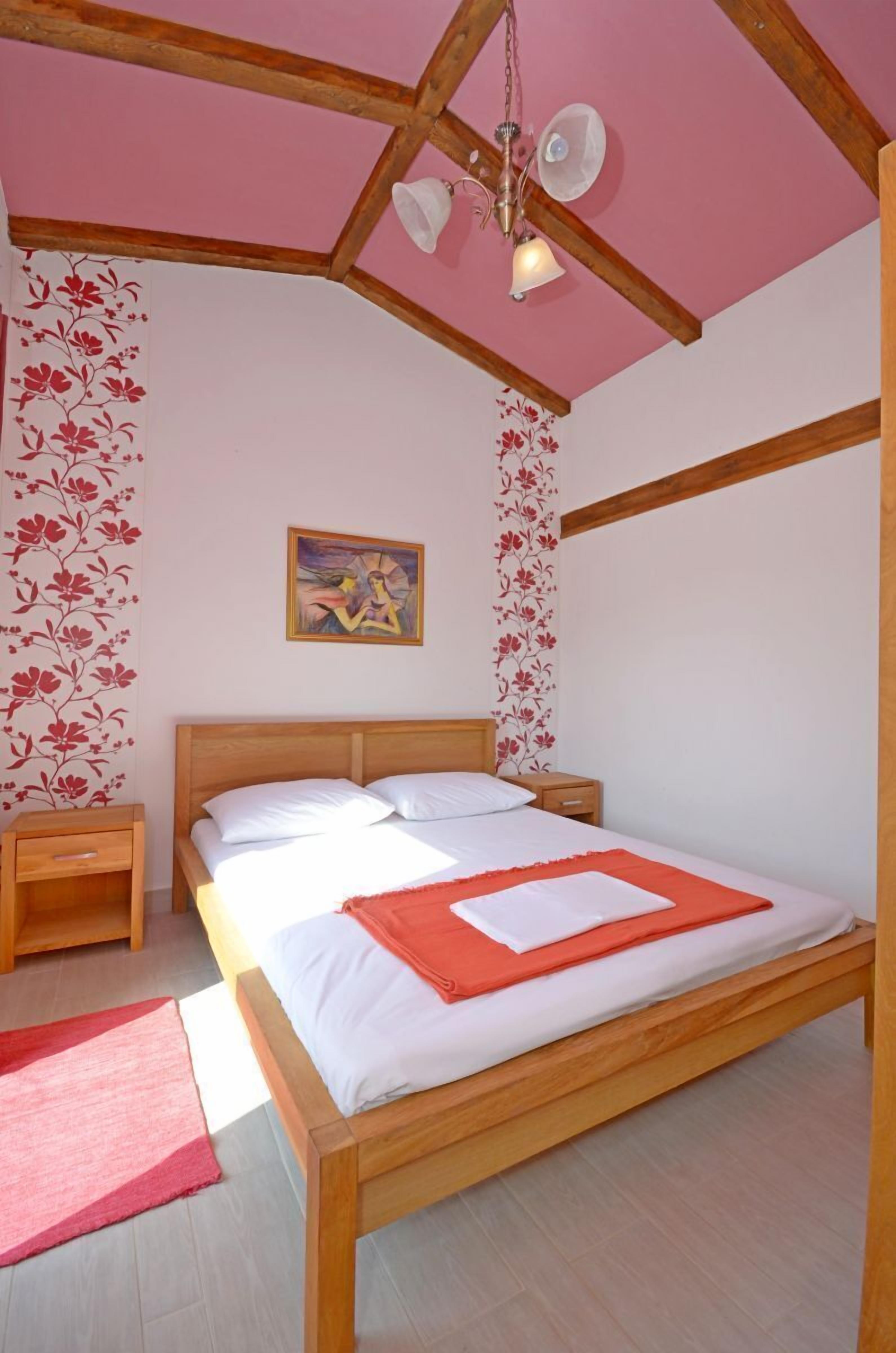 Una camera da letto con un letto in legno, un comodino, un tappeto rosso e carta da parati floreale.