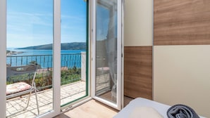 A room with a sliding glass door leading to a balcony with a view of the sea and hills. - Apartments Barbara (Poljica)
