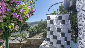 A courtyard with a checkered wall, a tree with pink flowers, and a view of the hills. - Apartments Barbara (Poljica)