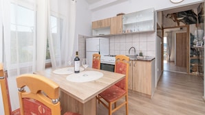 A modern kitchen with wooden cabinets, a white refrigerator, and a dining area with a table set for two. - Apartments Barbara (Poljica)
