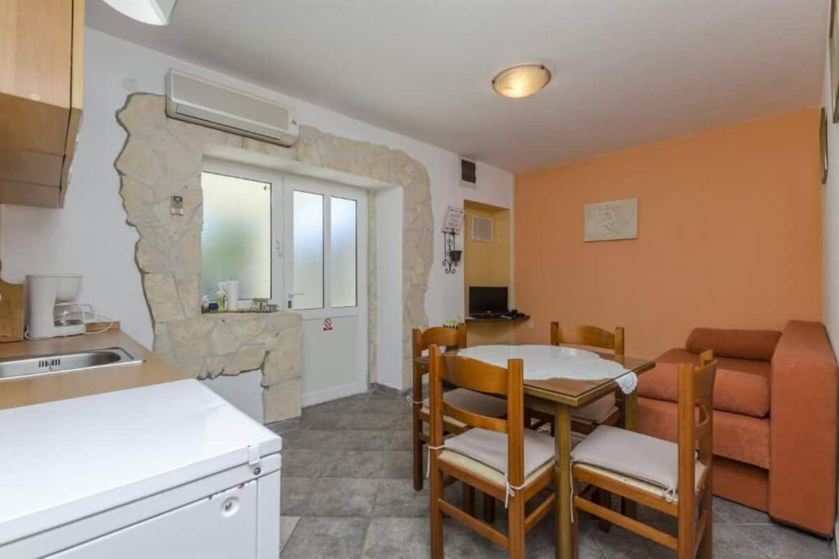 A compact kitchen with a stone wall, a dining area with wooden chairs, and a sofa.